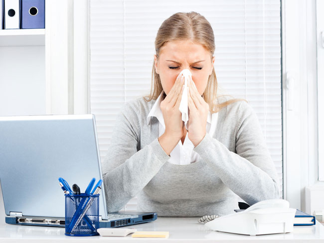 Woman at desk blowing nose