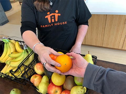 Person in Family House shirt hands out fruit