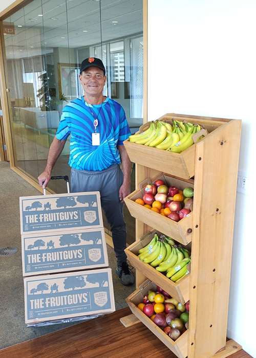 Man delivering FruitGuys boxes next to office fruit stand