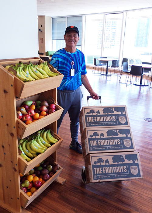 Man delivering FruitGuys boxes next to office fruit stand