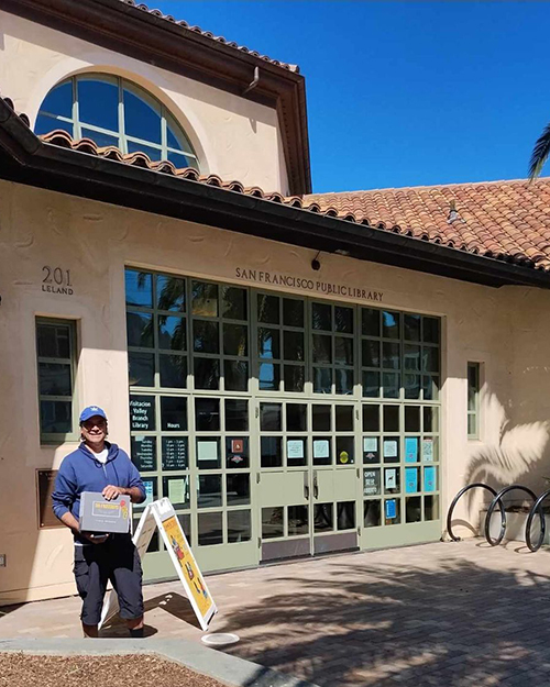 Man standing in front of the San Francisco Public Library holding a The FruitGuys box