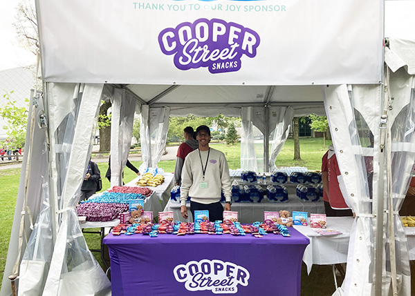 Cooper Street Snacks booth full of Granola Bakes, Thank You To Our Joy Sponsor on booth banner