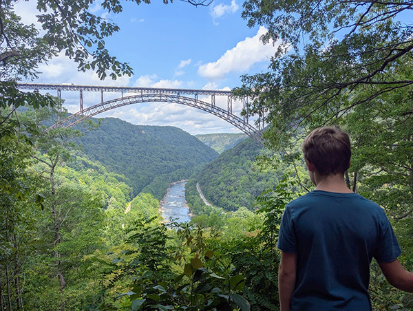 Boy overlooking bridge over river in valley