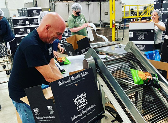 Man unloading box in production facility with workers behind him