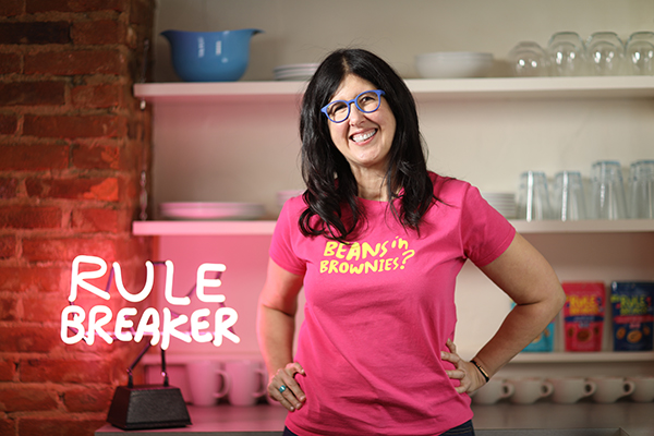 Woman wearing Rule Breaker shirt in front of Rule Breaker neon sign