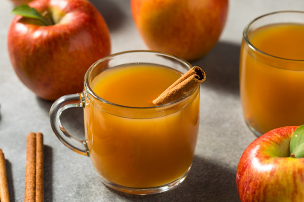 Glasses of apple cider surrounded by cinnamon sticks and apples