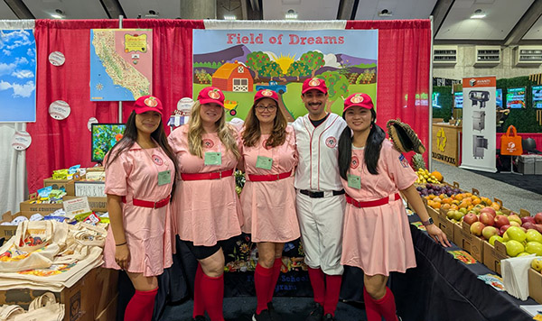 Smiling school team in CSNA booth, Field of Dreams banner in the background