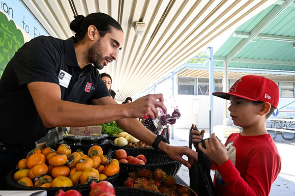 Man at school farmers market handing bag of sliced fruit to student