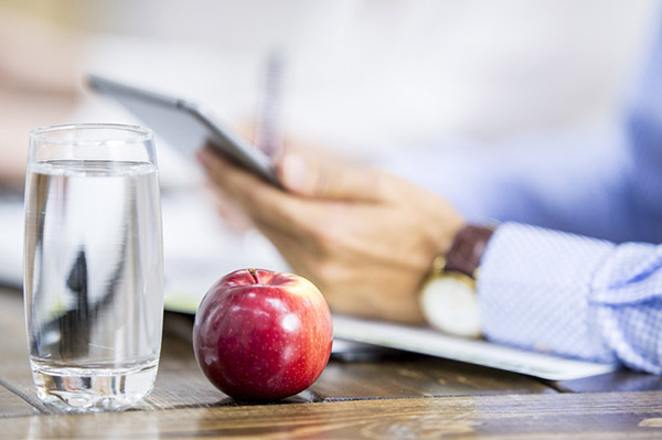 Apple and water glass sit beside man working