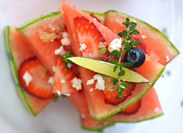 Watermelon slices sprinkled with herbs, cheese, berries, and finger limes