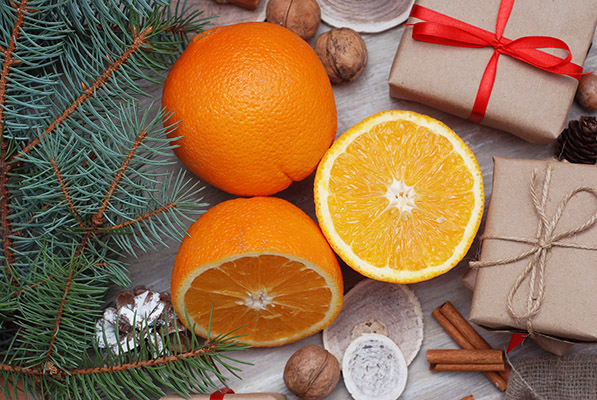 Gift box in kraft paper with bow, pinecones, oranges fruit, cinnamon, nuts on wooden background