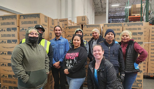 Group of smiling people in a warehouse standing in front of The FruitGuys boxes