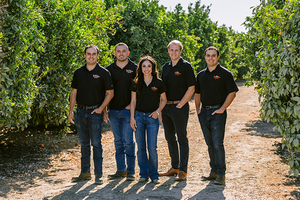 Four men and one woman posing in an orchard