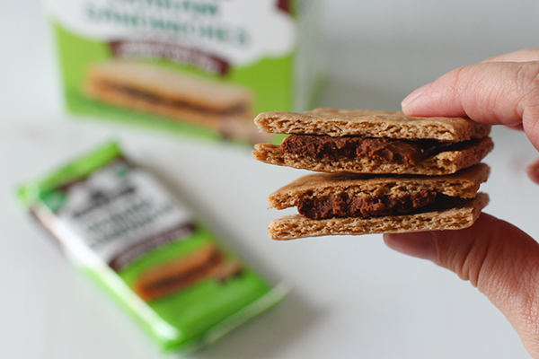 Hand holding chocolate peanut butter graham sandwiches in front of more packaged sandwiches