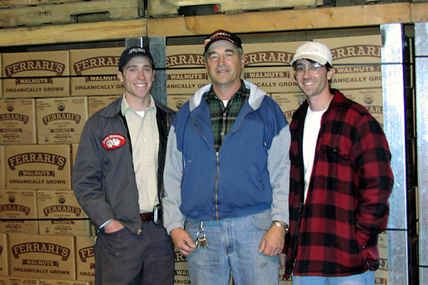 Three smiling men in front of boxes of walnuts