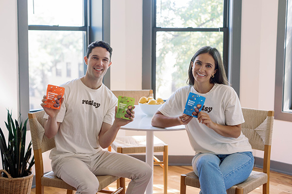 Smiling man and woman at a table holding realsy snacks