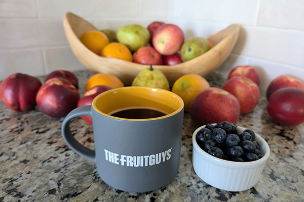 Cup of coffee with The FruitGuys logo surrounded by fresh fruit