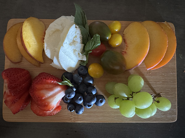 Charcuterie board with fresh fruit, cherry tomatoes, cheese, and basil
