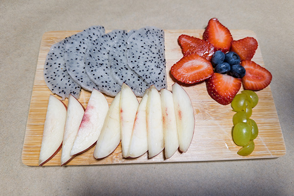 Charcuterie board of fresh fruit, including strawberry slices shaped like a flower with a grape stem and blueberry center