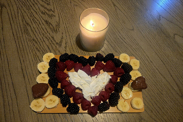 Charcuterie board with fruit arranged in a heart shape, sitting next to a candle