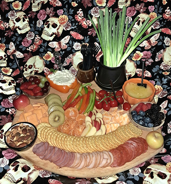 Charcuterie board with fruit, meat, cheese, crackers, dips, silverware, nuts and green onions