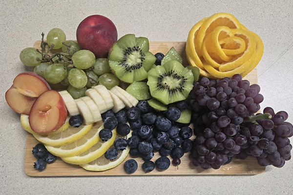 Charcuterie board overflowing with colorful fruit, including an orange rose and kiwi flowers