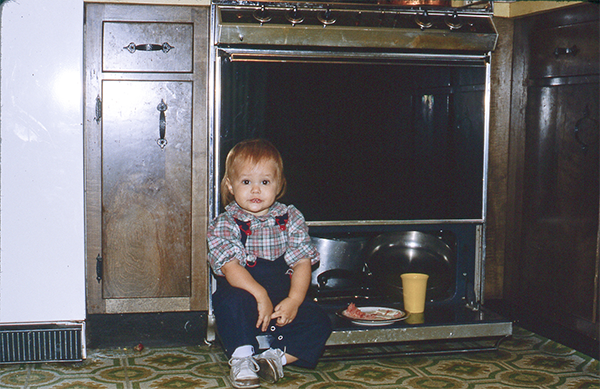 Small child eating sitting on a cabinet door eating a snack