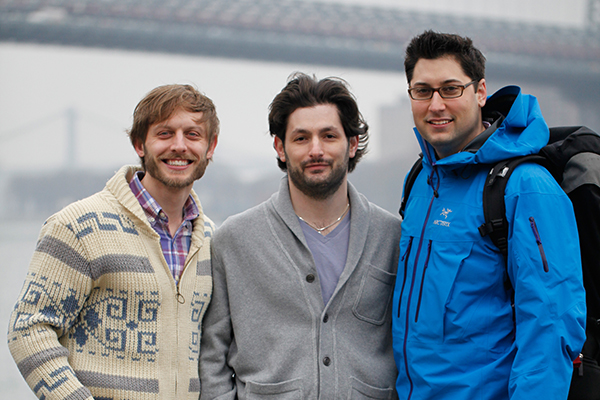 Three men smiling in front of a bridge