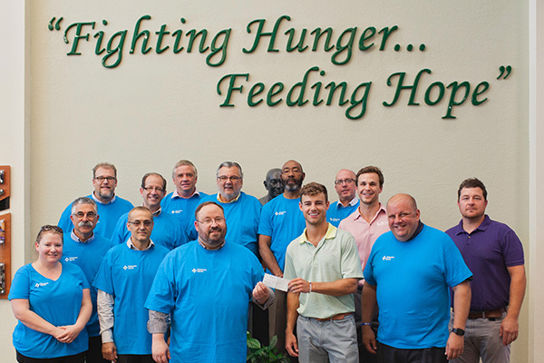 Group of people under a Fighting Hunger...Feeding Hope sign, one man handing over a check