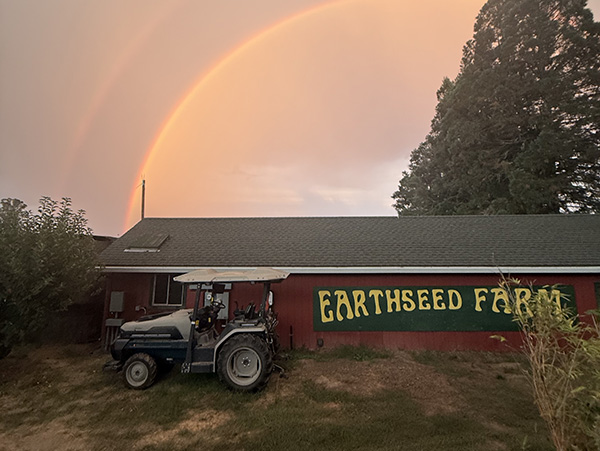 Farm building with Earthseed Farm sign, tractor in foreground with rainbow behind building
