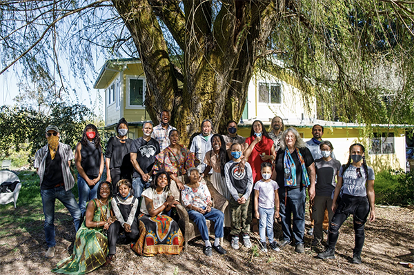 Large group of people smiling in front of a tree and farmhouse