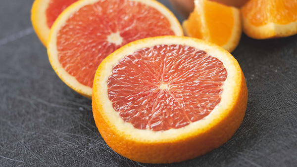 Sliced pink-fleshed orange, orange-fleshed oranges in the background