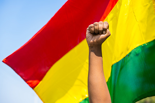 Black person's fist raised against a red, yellow, and green striped flag