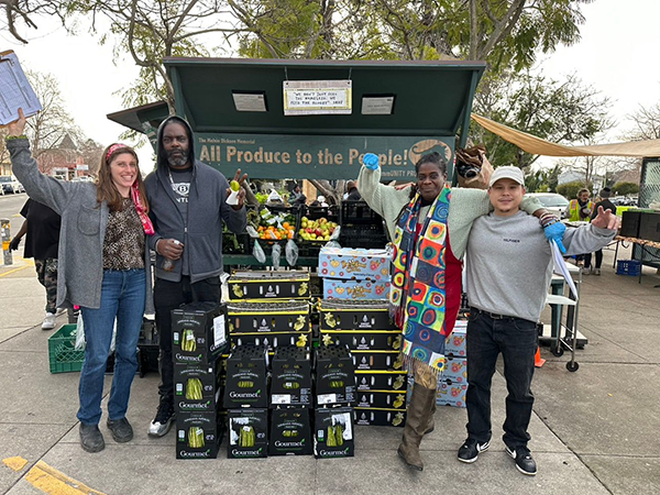 Group of people standing in front of a stand of fresh fruit