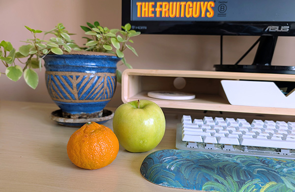 Office desk with fresh fruit, a plant, a keyboard, and a computer visible