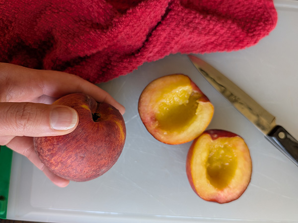 hands cutting peaches on a cutting board, with a towel beside