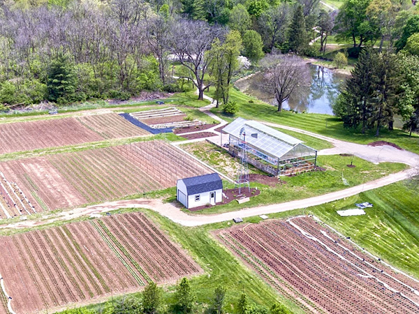 Farm overhead view showing rows of crops, a farmhouse, and a large solar powered greenhouse