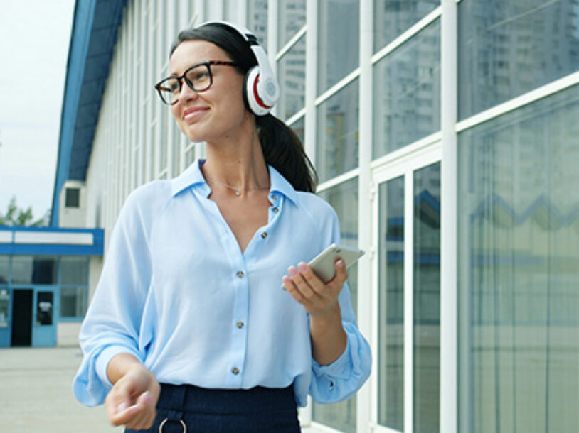 Woman office worker taking a walk outside with headphones; coworker in the background