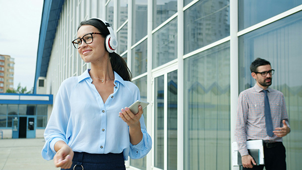 Woman office worker taking a walk outside with headphones; coworker in the background