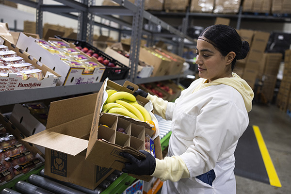 Woman working on a fruit packing line holding a FruitGuys box