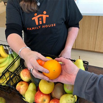 Family House Donation Hands Fruit Person in Family House shirt hands out fruit